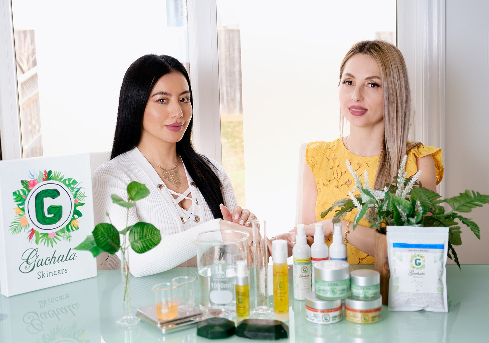 Two women showcasing Gachala Skincare's luxurious organic products at a bright, elegant setting, surrounded by Amazonian-infused creams, serums, and oils, emphasizing clean beauty and eco-conscious rituals"